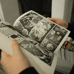 Des mains tiennent un manga ouvert, révélant des cases de bande dessinée pleines d'action. Apprendre comment lire un manga est facile avec ces images dynamiques.