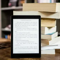 Liseuse affichant un roman, à côté d'une pile de livres. Idéal pour trouver un epub gratuit sans inscription et plonger dans une nouvelle histoire.