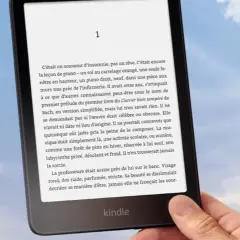 Main tenant un Kindle, un livre numérique de Nextory, sur fond de ciel bleu et nuageux.