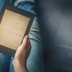 Personne lisant un livre sur une tablette ou liseuse, confortablement installée dans son jean.