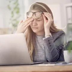 Une jeune femme, liseuse, se frotte les yeux fatigués devant son ordinateur.