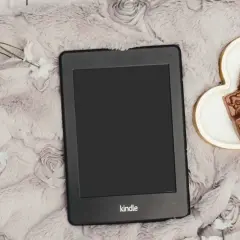 Un Kindle Vella posé sur une couverture douce, avec des chocolats en forme de cœur et des fleurs blanches.