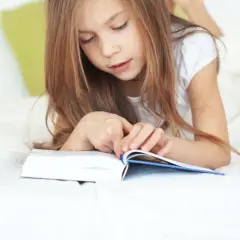 Une jeune fille de 11 ans, allongée sur un lit, est absorbée par la lecture d'un livre.