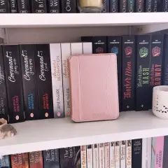 Une liseuse Kobo rose est bloquée en veille, posée sur une étagère remplie de livres.
