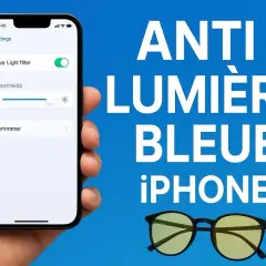 Une main tient un iPhone affichant le filtre anti lumière bleue activé. Des lunettes jaunes sont posées à côté.