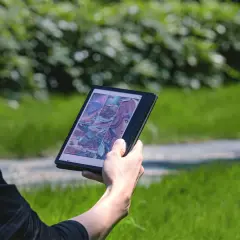 Une personne lit une bande dessinée de science-fiction sur une liseuse Boox dans un parc verdoyant.