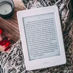 Un ebook Fnac sur Kindle, posé sur une couverture douillette, avec des feuilles rouges et une bougie.