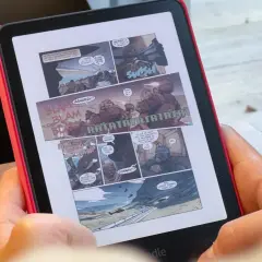 Une personne lit une bande dessinée d'action sur un cbz kindle. Des onomatopées comme "BLAM" et "RATATATA" parsèment les cases.