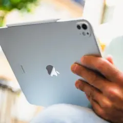 Un homme est assis dehors, profitant d'un moment pour lire sur son iPad.