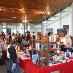 Foule dans un salon littéraire, admirant des livres et des affiches.