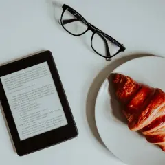 Un e-reader, des lunettes et un croissant sur une assiette. Idéal pour créer un epub et s'évader dans une histoire.