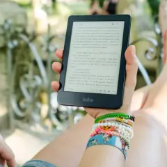 Une personne lit un ebook Kobo dans un jardin, profitant d'un moment de détente avec une collection de 1001 ebooks légal.