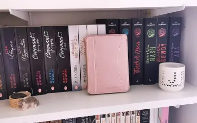 Une liseuse Kobo rose est bloquée en veille, posée sur une étagère remplie de livres.
