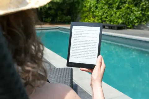 Une personne lit un epub en ligne au bord d'une piscine, profitant du soleil et d'une lecture immersive.