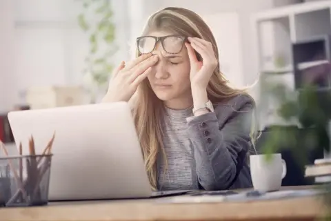 Une jeune femme, liseuse, se frotte les yeux fatigués devant son ordinateur.
