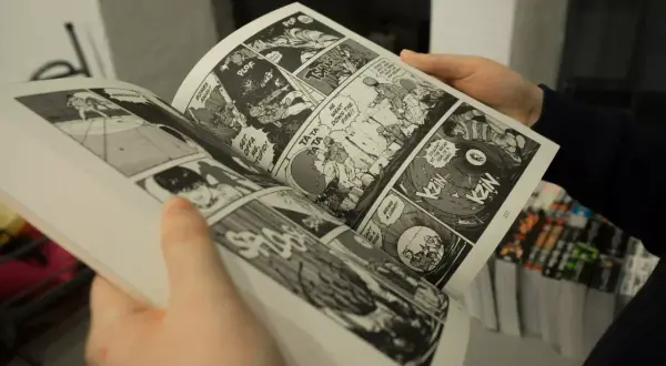 Des mains tiennent un manga ouvert, révélant des cases de bande dessinée pleines d'action. Apprendre comment lire un manga est facile avec ces images dynamiques.