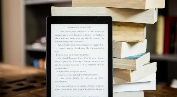 Liseuse affichant un roman, à côté d'une pile de livres. Idéal pour trouver un epub gratuit sans inscription et plonger dans une nouvelle histoire.