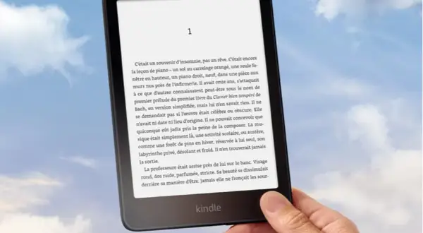 Main tenant un Kindle, un livre numérique de Nextory, sur fond de ciel bleu et nuageux.
