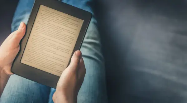 Personne lisant un livre sur une tablette ou liseuse, confortablement installée dans son jean.