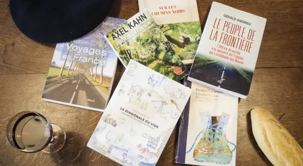 Un béret, un verre de vin, une baguette et plusieurs livres sur la France, dont "Voyages en France" et "La Diagonale du vide", parfaits pour un récit de voyage.