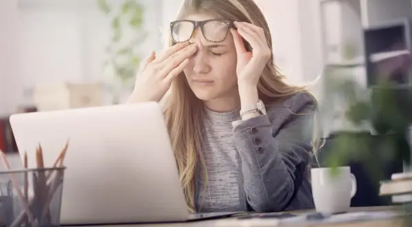 Une jeune femme, liseuse, se frotte les yeux fatigués devant son ordinateur.