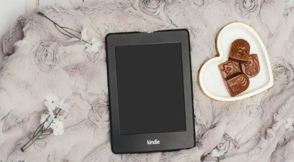 Un Kindle Vella posé sur une couverture douce, avec des chocolats en forme de cœur et des fleurs blanches.