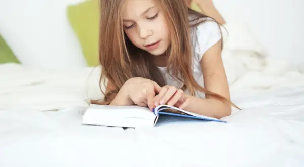 Une jeune fille de 11 ans, allongée sur un lit, est absorbée par la lecture d'un livre.