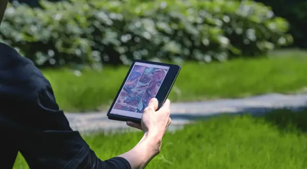 Une personne lit une bande dessinée de science-fiction sur une liseuse Boox dans un parc verdoyant.