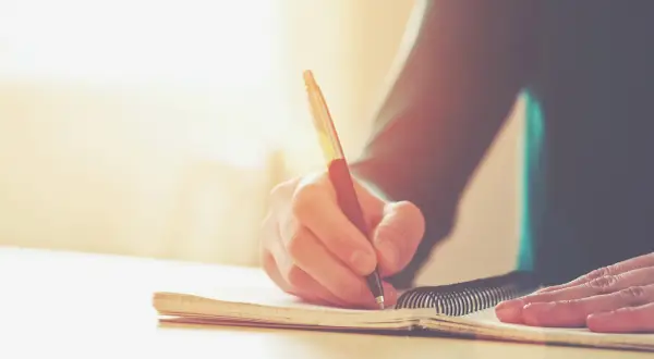 Main d'une personne écrivant dans un carnet. Une histoire vraie prend forme, un témoignage précieux consigné dans ce livre.