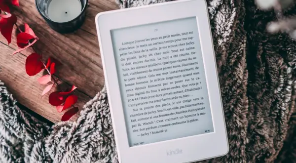 Un ebook Fnac sur Kindle, posé sur une couverture douillette, avec des feuilles rouges et une bougie.
