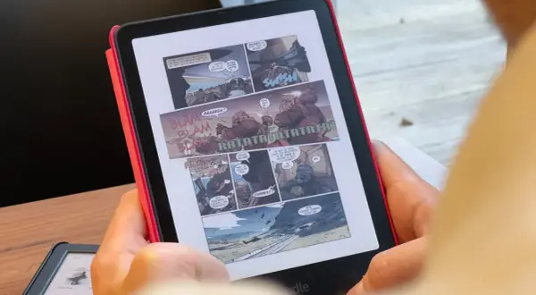 Une personne lit une bande dessinée d'action sur un cbz kindle. Des onomatopées comme "BLAM" et "RATATATA" parsèment les cases.