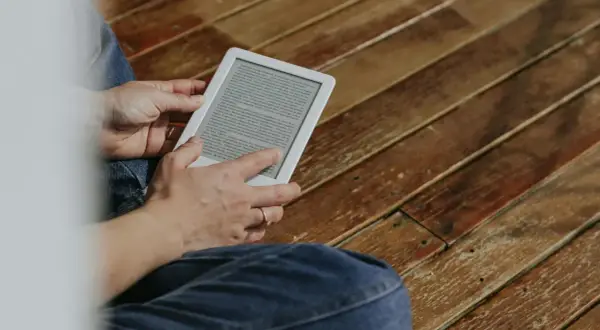 Une personne lit sur une tablette encre électronique, assise sur un plancher en bois.