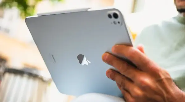 Un homme est assis dehors, profitant d'un moment pour lire sur son iPad.