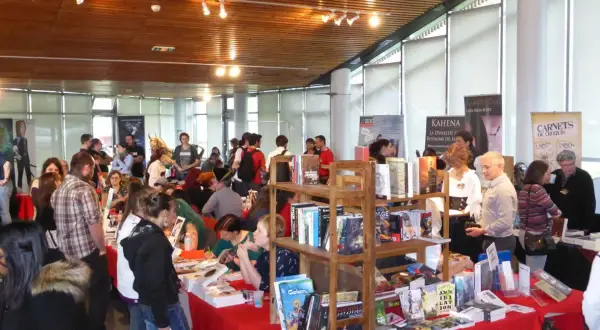 Foule dans un salon littéraire, admirant des livres et des affiches.