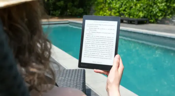 Une personne lit un livre électronique Kobo au bord d'une piscine, profitant du soleil. Un excellent choix pour un epub reader sur Ubuntu.