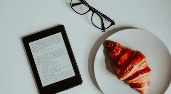 Un e-reader, des lunettes et un croissant sur une assiette. Idéal pour créer un epub et s'évader dans une histoire.