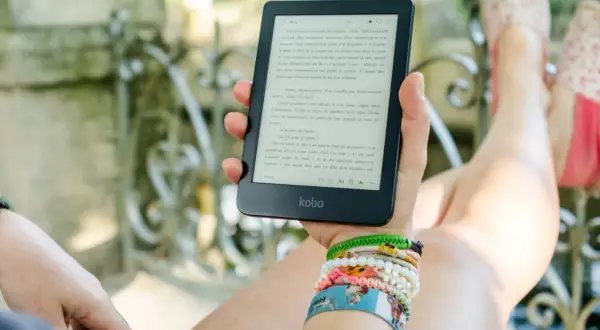 Une personne lit un ebook Kobo dans un jardin, profitant d'un moment de détente avec une collection de 1001 ebooks légal.