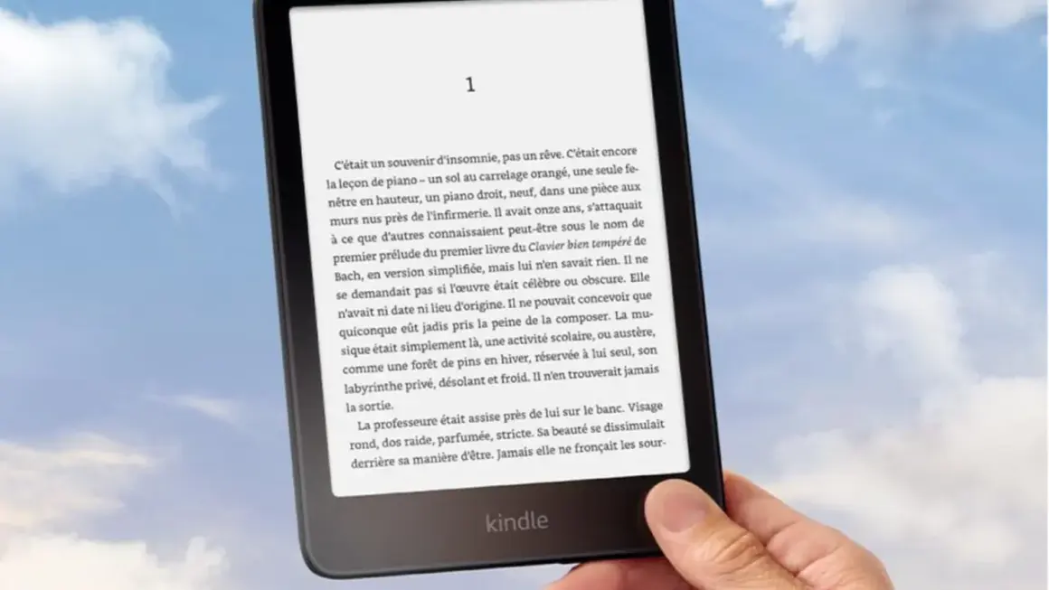 Main tenant un Kindle, un livre numérique de Nextory, sur fond de ciel bleu et nuageux.