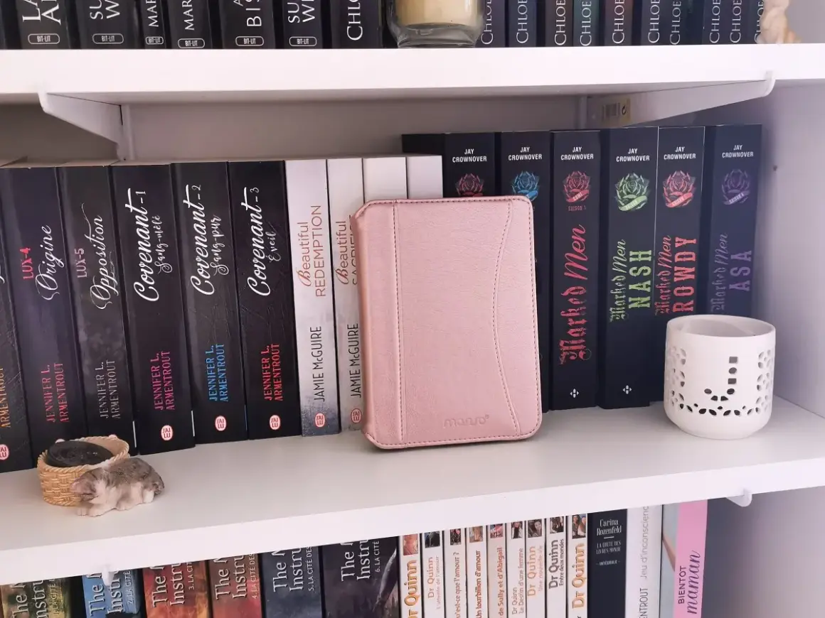Une liseuse Kobo rose est bloquée en veille, posée sur une étagère remplie de livres.