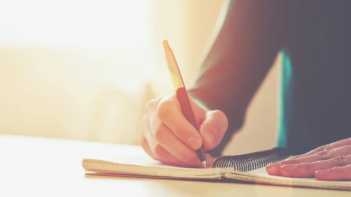 Main d'une personne écrivant dans un carnet. Une histoire vraie prend forme, un témoignage précieux consigné dans ce livre.