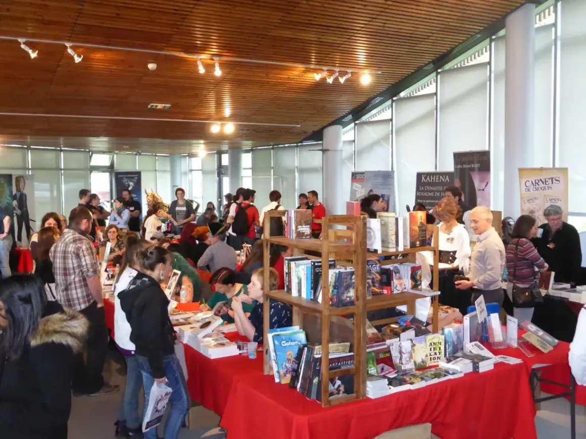 Foule dans un salon littéraire, admirant des livres et des affiches.