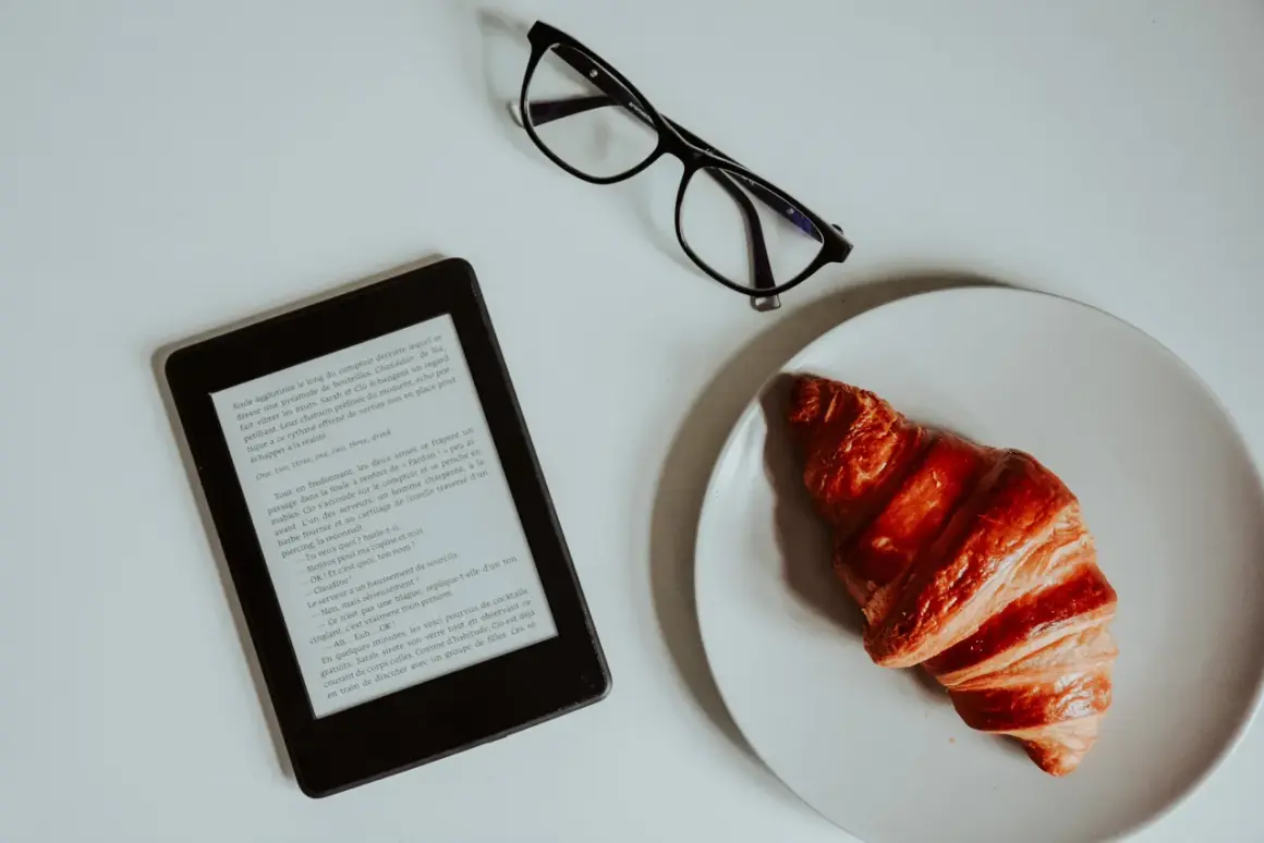 Un e-reader, des lunettes et un croissant sur une assiette. Idéal pour créer un epub et s'évader dans une histoire.