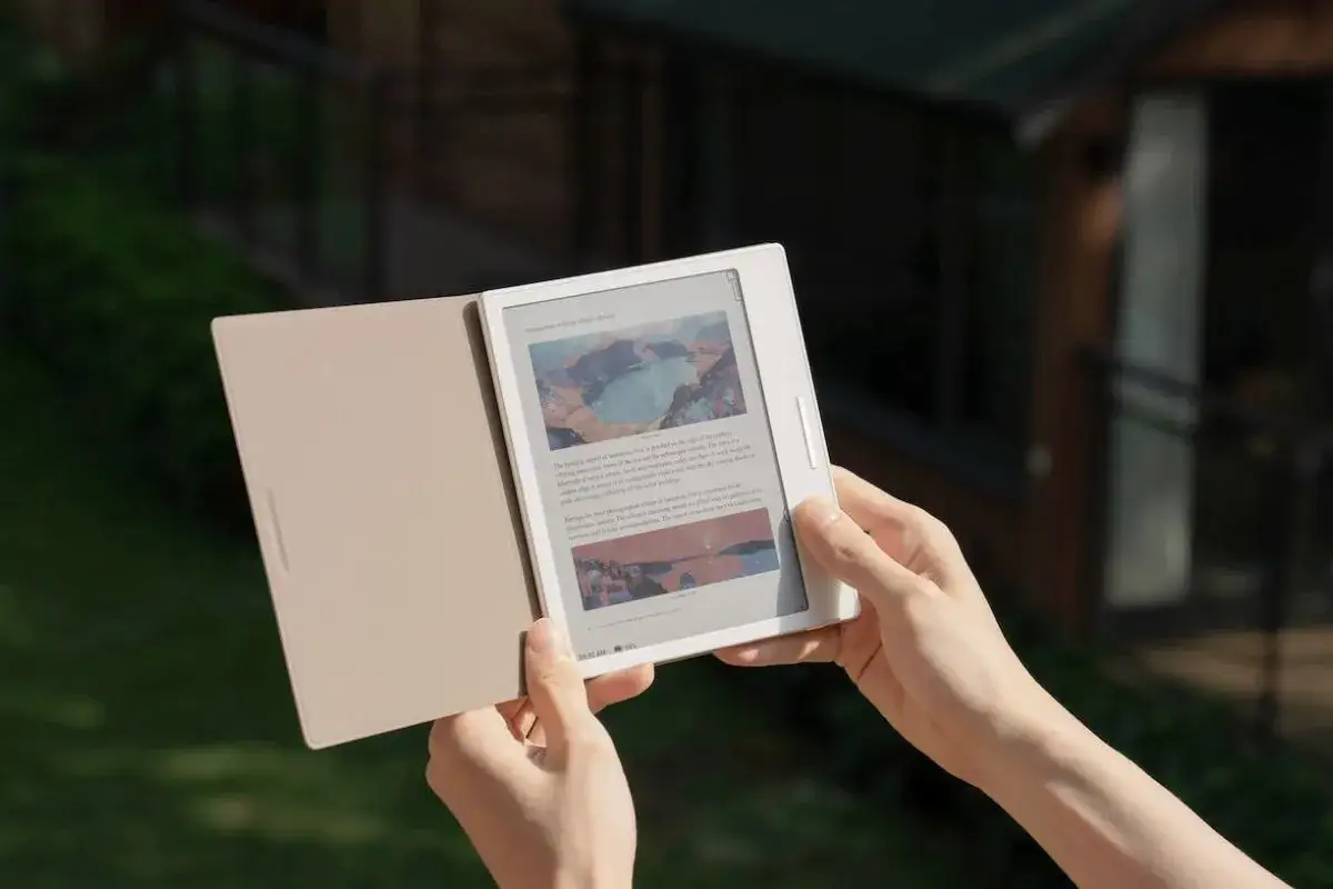 Mains tenant une liseuse Boox avec sa couverture ouverte, affichant des images et du texte.