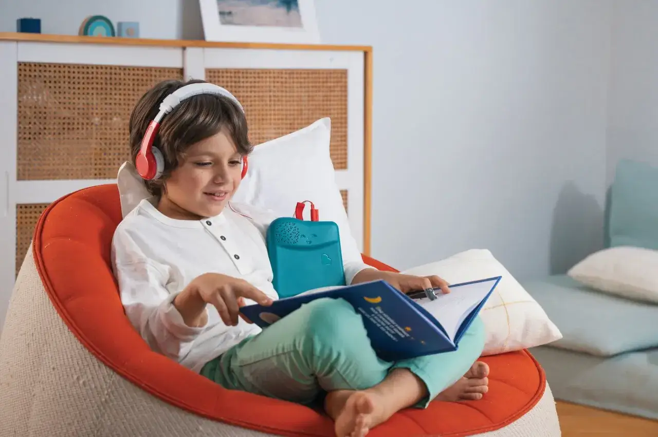 Un garçon écoute un livre audio jeunesse, confortablement installé. Un appareil bleu est posé sur ses genoux.