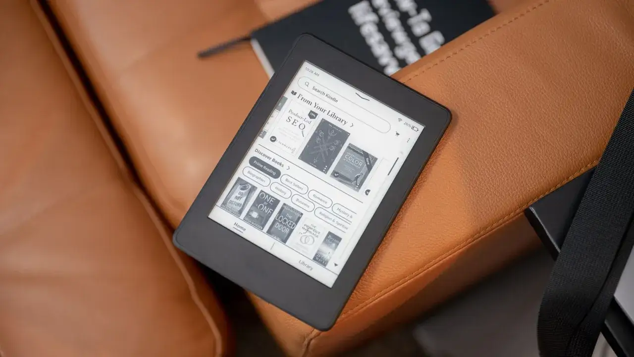 Lisez vos livres pr&eacute;f&eacute;r&eacute;s sur ce Kindle, qui affiche des titres en format epub. Il est pos&eacute; sur un canap&eacute; en cuir marron.