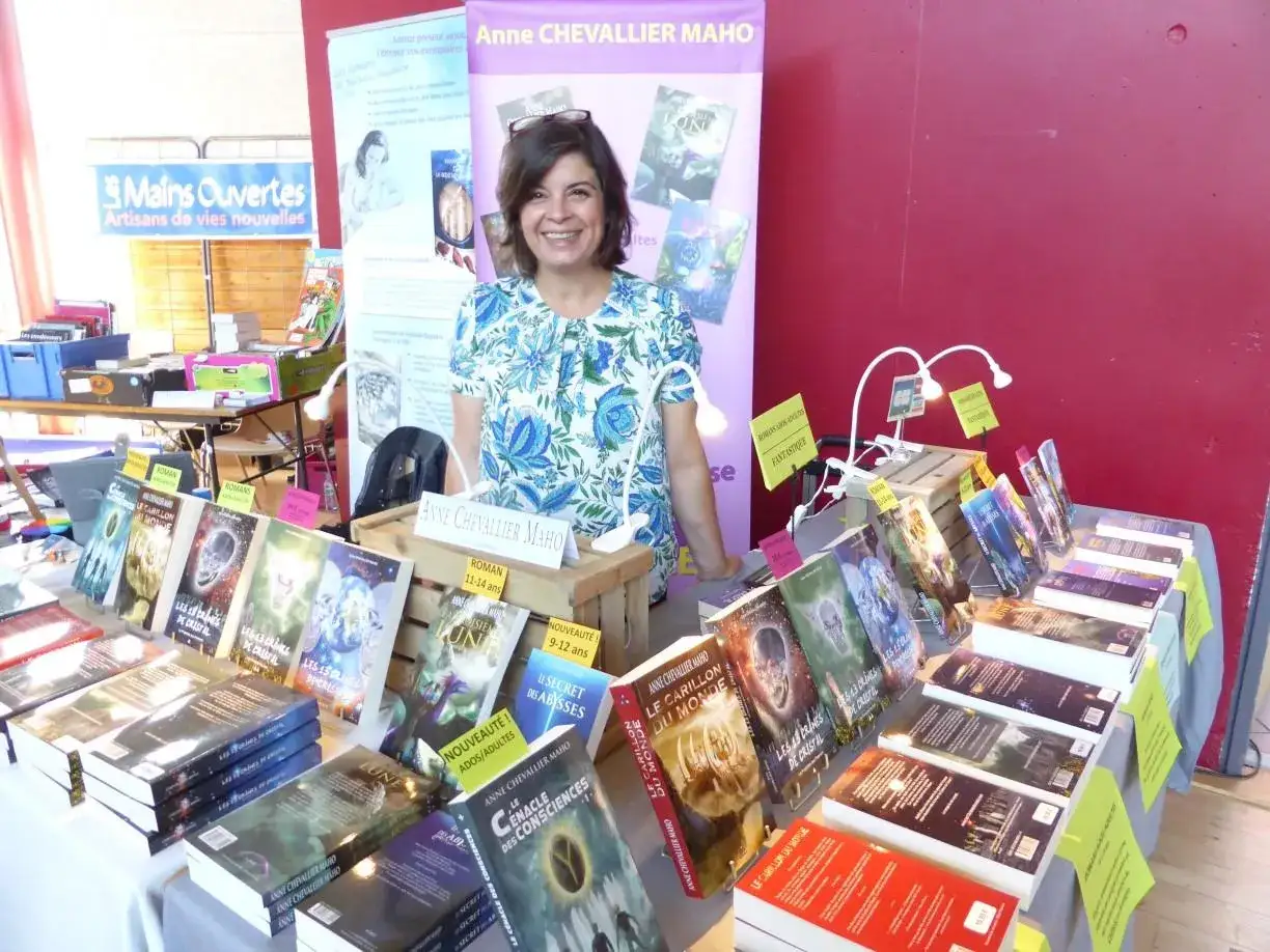 Une autrice souriante présente son salon littéraire, entourée de ses romans fantastiques et de science-fiction.