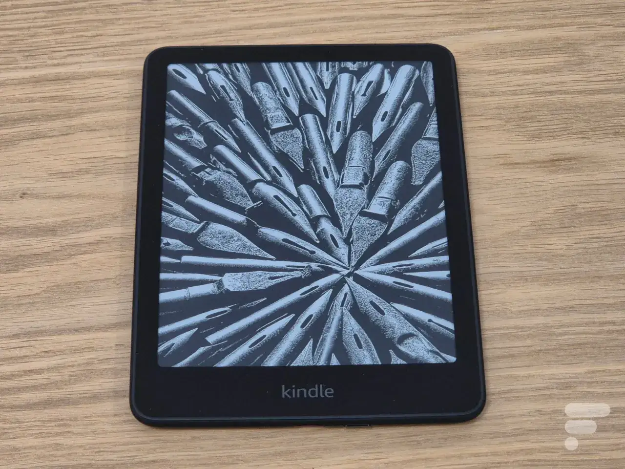 Un kindle reconditionn&eacute; avec un &eacute;cran affichant une image abstraite de plumes d'encre, pos&eacute; sur un fond en bois.