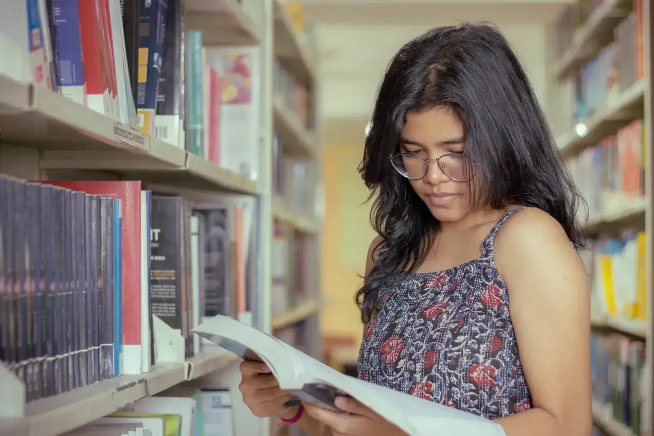 Une jeune femme choisit un livre dans une bibliothèque, peut-être à la recherche du top 10 des livres pour adolescent.