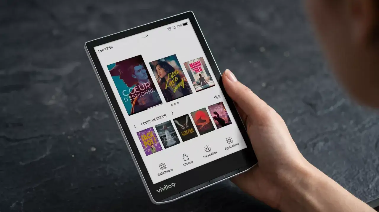 Une main tient une liseuse vivlio light hd color affichant des couvertures de livres.