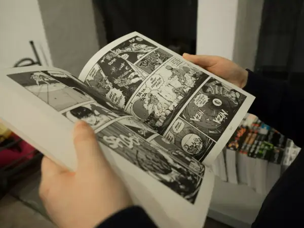 Des mains tiennent un manga ouvert, révélant des cases de bande dessinée pleines d'action. Apprendre comment lire un manga est facile avec ces images dynamiques.